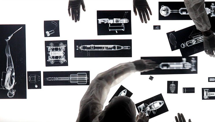 Hands interacting with a wall displaying multiple x-ray images of various objects and human skeletons.