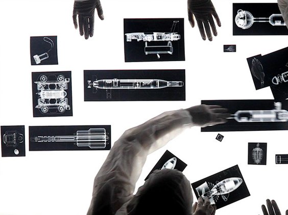 Hands interacting with a wall displaying multiple x-ray images of various objects and human skeletons.