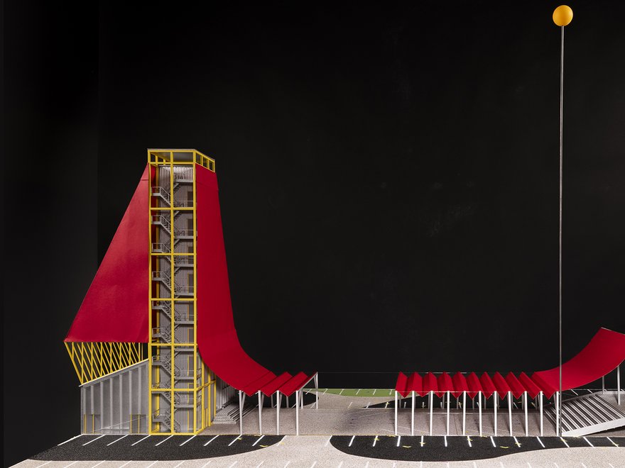 An architectural rendering of a modern structure featuring a long, red, undulating slide-like element that connects a tall, yellow framed tower on the left to a lower building on the right.