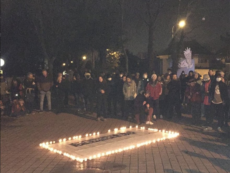 A crowd of people stand around a rectangle of candles