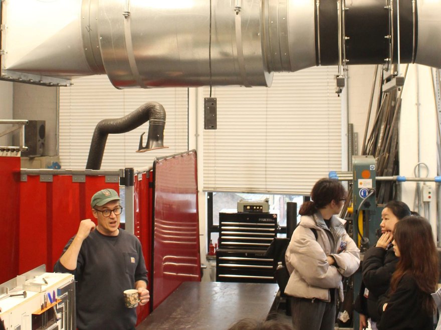 A man stands in a room with big extractor fans talking to a group of people