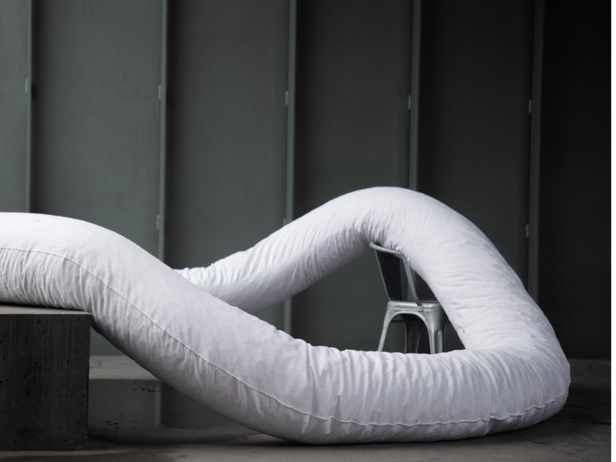 A sculpture made of a large white stuffed fabric tube, draped over stairs and a chair