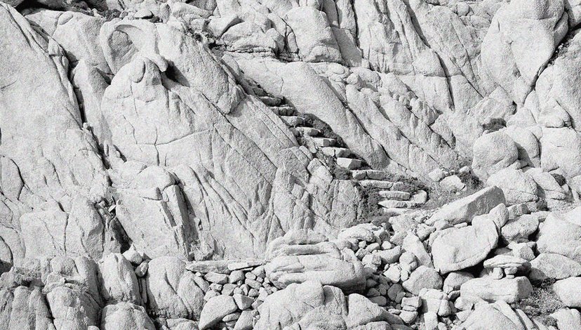 A black and white photo of rock stairs built into a rugged, rocky cliffside in Sardinia, Italy, designed by architect Alberto Ponis