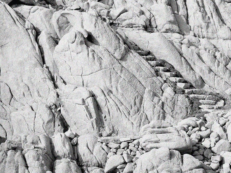 A black and white photo of rock stairs built into a rugged, rocky cliffside in Sardinia, Italy, designed by architect Alberto Ponis
