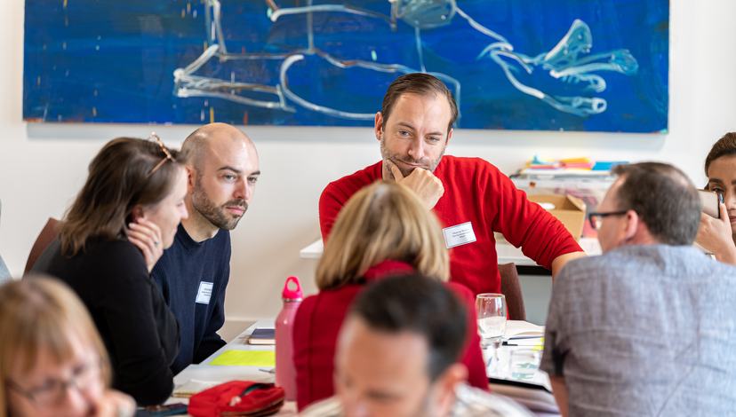 Participants of Creative Leadership workshop gathered around a table, discussing their ideas.