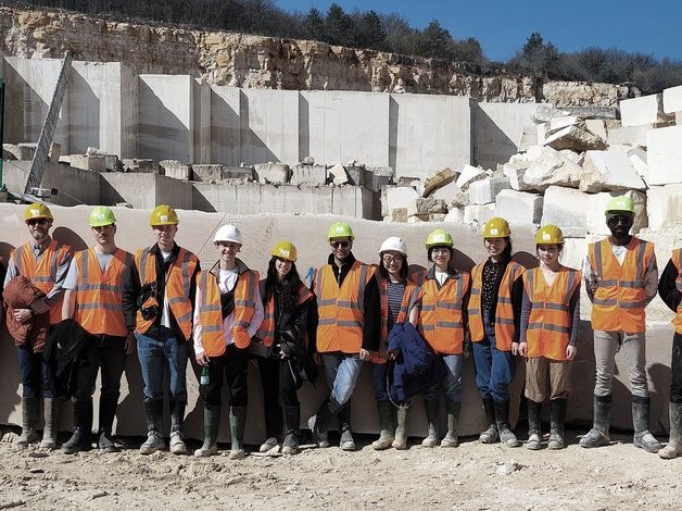 A group of students wearing high vis and safety helmets stand in a stone quarry