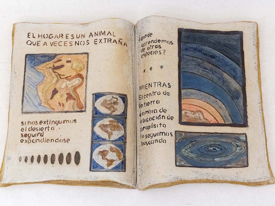 A ceramic book lays open with pictures Spanish text inside