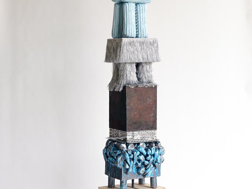 Tall totem sculpture made of stacked textured blocks topped with a red ceramic head.