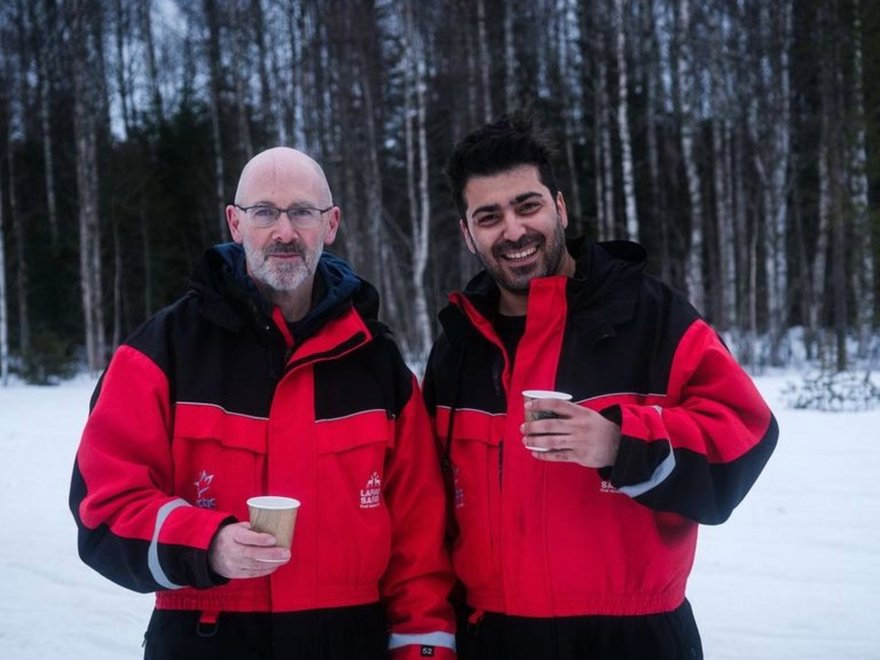 two men smile together in snow suits in the snow