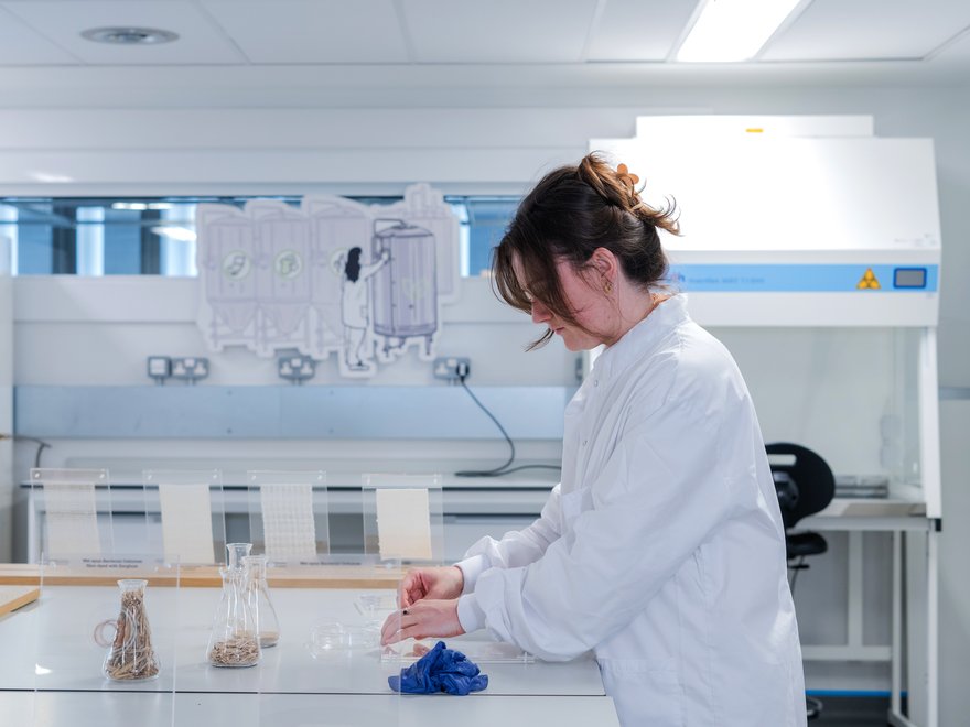 A woman in a lab coat preparing samples in flasks.