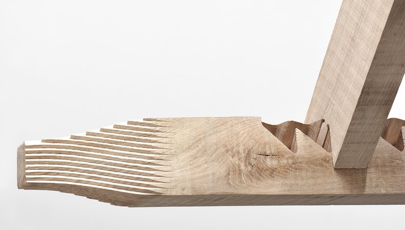 A close-up of a wooden object with a stepped, textured surface on the left, transitioning to a wavy, carved section in the middle, and a smooth, angled piece of wood extending upwards from the right.