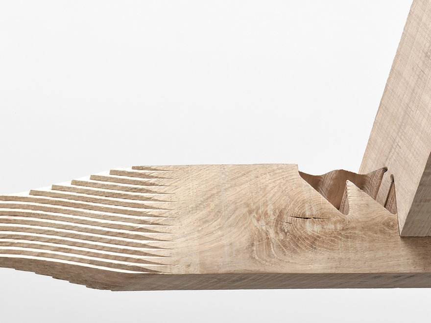 A close-up of a wooden object with a stepped, textured surface on the left, transitioning to a wavy, carved section in the middle, and a smooth, angled piece of wood extending upwards from the right.