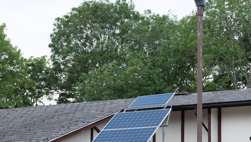 A grey minivan parked in a driveway next to a house with solar panels on its roof, with a street lamp visible on the right.