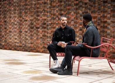 Two students sit on benches outside the Royal College of Art