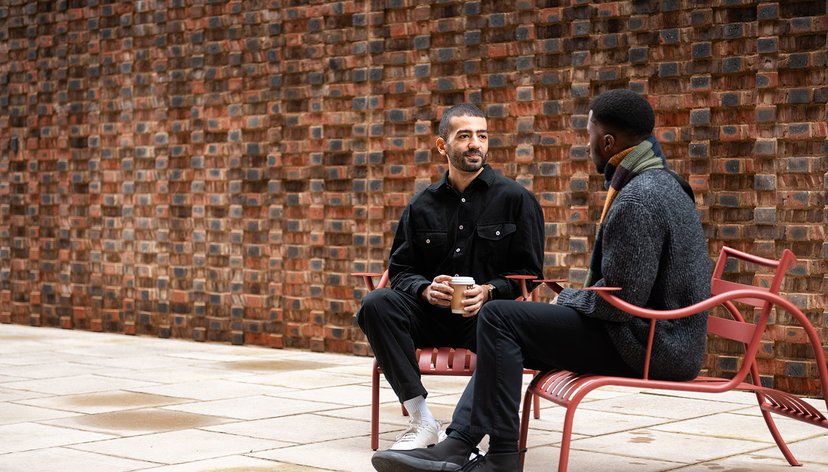 Two students sit on benches outside the Royal College of Art