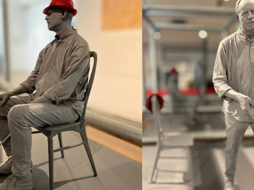 Sculpture of artist David Johnson, depicted as a blind man with a red hat and white cane, shown in two views: seated and standing.