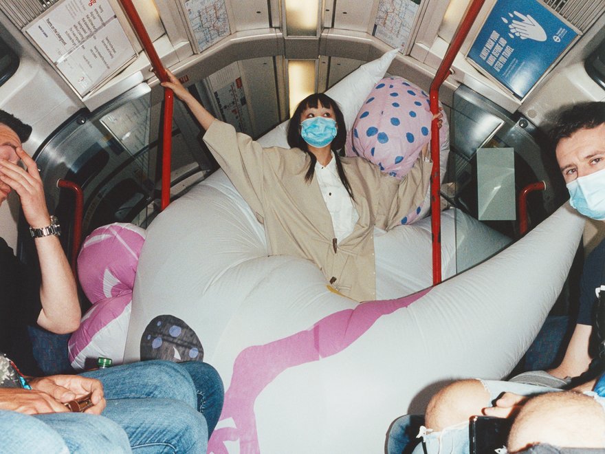 The artist and passengers on a London underground train, with a large white and pink inflatable sculpture wrapped around their body and filling the carriage.