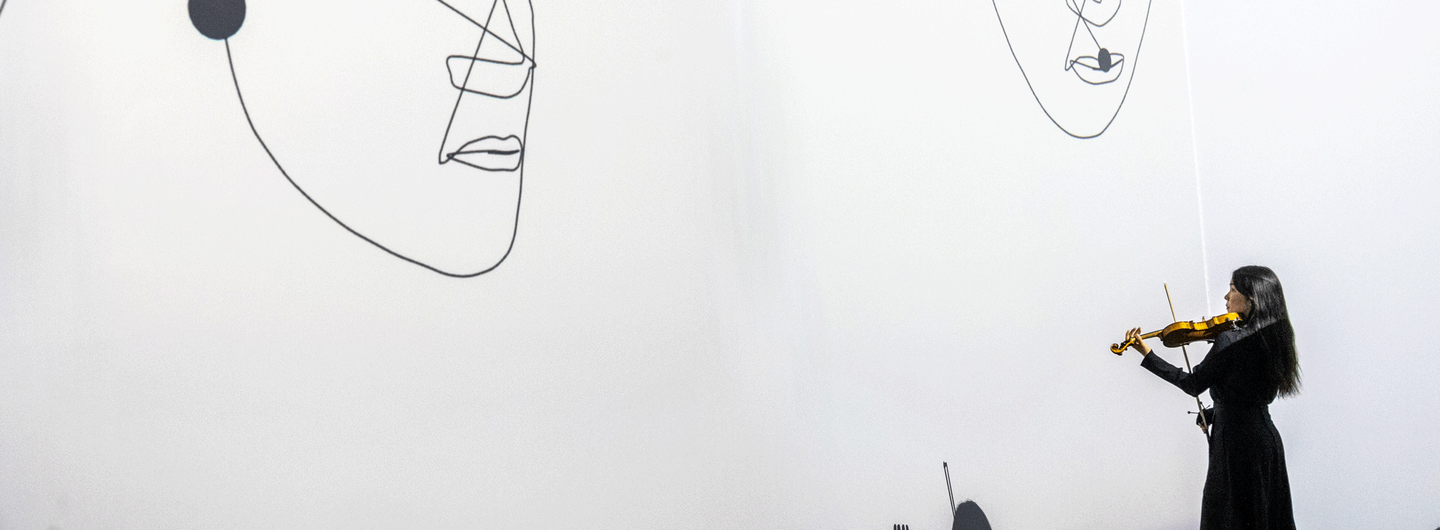 Sue-In Kang performing violin within a responsive visual environment, where projected faces emerge and change in response to the live performance. Photo: Vivaan Thongram