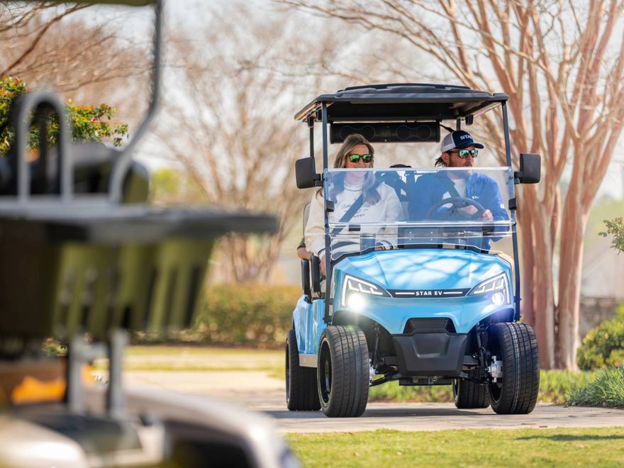a man and woman drive a golf buggy in a sunny park