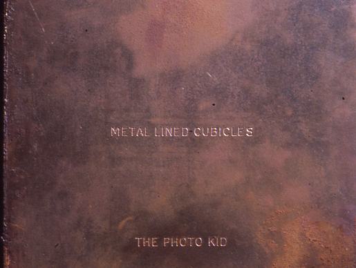 An aged, rust-colored book cover with a weathered, metallic texture. The title "METAL-LINED CUBICLES" is printed in small, white, all-caps serif font in the centre, with the author name "THE PHOTO KID" positioned below it.