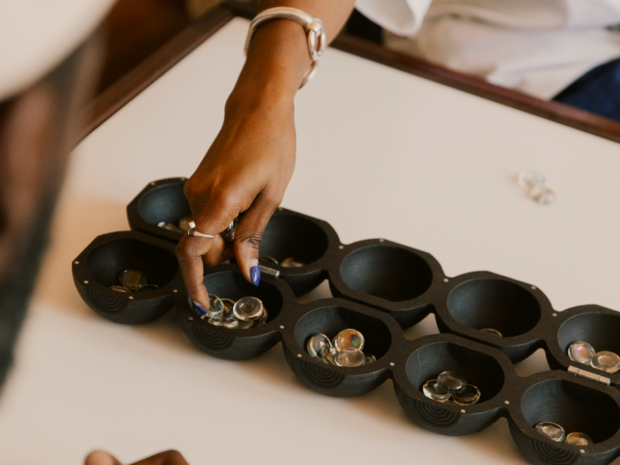 Close-up of hands playing Nchọ, a traditional Mancala board game with glass seeds.