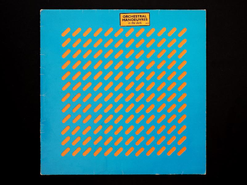 The self-titled debut album cover for Orchestral Manoeuvres in the Dark, featuring a blue background with a grid of orange, diagonal, pill-shaped die-cuts.