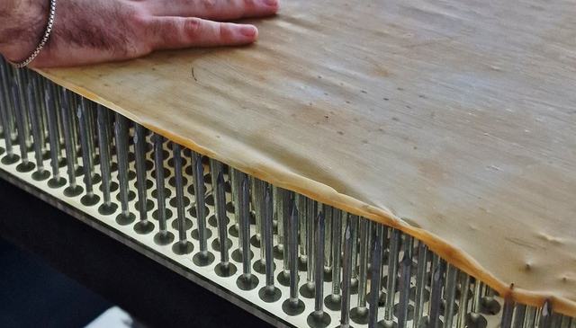 A hand rests on a sheet of latex over a bed of nails