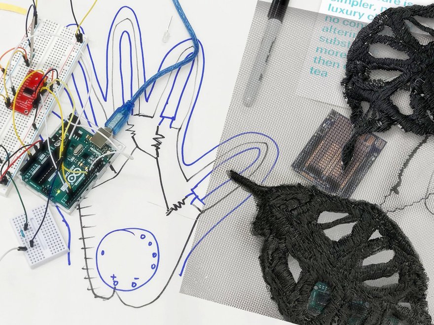 Close up detail of a motherboard and wires against sketches for a robotic hand.
