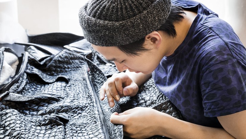 A student in a knitted hat hand sews a garment made of black faux crocodile leather