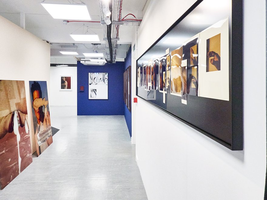 Installation view of exhibition, with large painted canvases hanging in a corridor and propped against a wall.