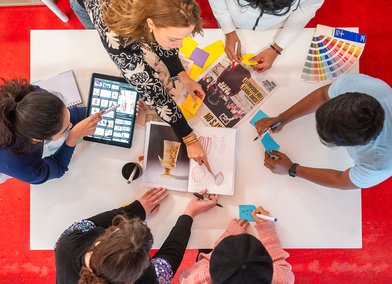 A group of RCA students collaborate on a creative project with pens and post it notes around a table