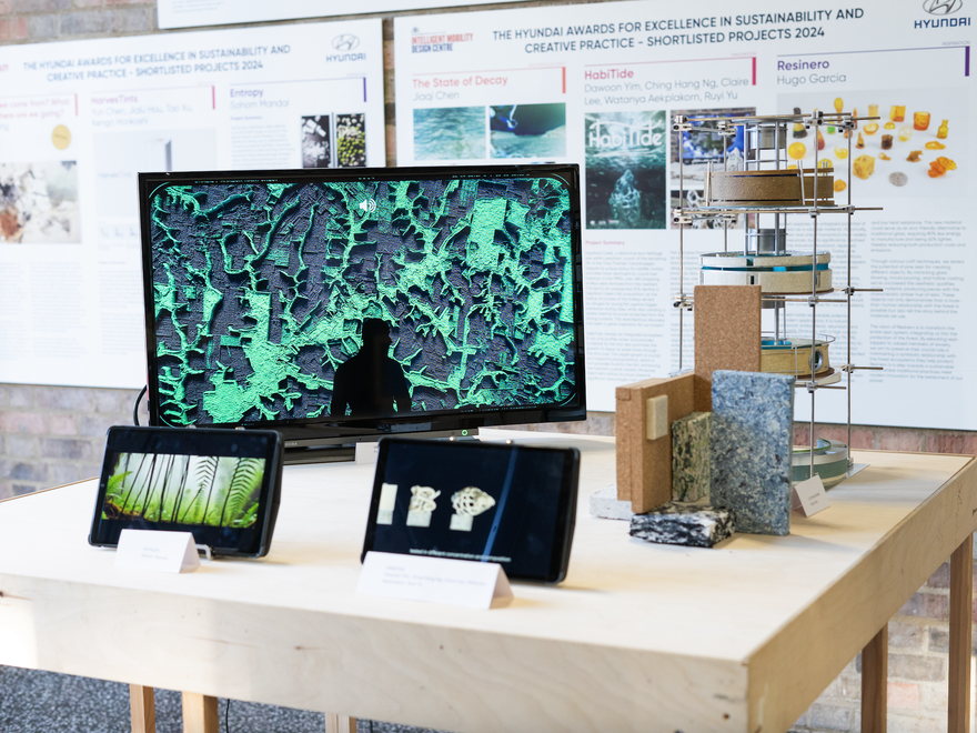 A wood table covered with a group of objects, including two iPads and a large screen showing an image of a man standing in front of a deforested rainforest