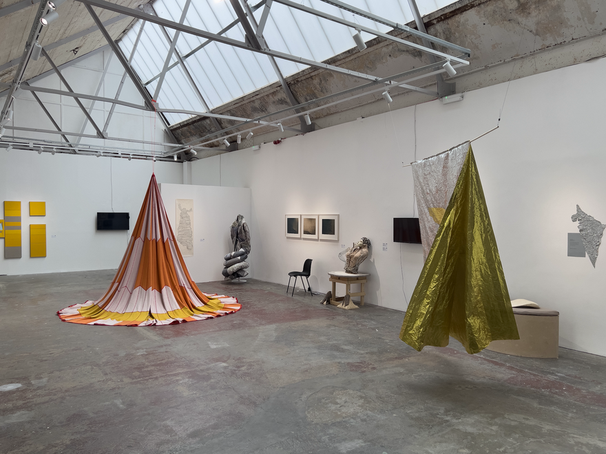 A large gallery space with two large pieces of fabric hanging from the ceiling in the shape of tents.