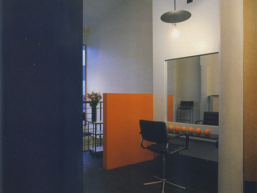 An image of a modern interior space, likely a hair salon or studio, featuring a black salon chair facing a large wall mirror.