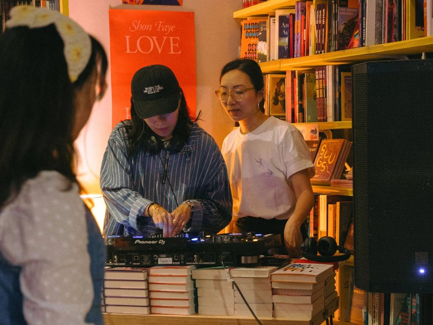 Two women dj to a crowd in a book store