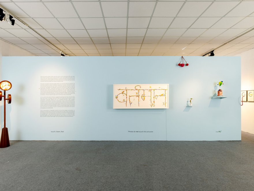 Installation view of the Vartaman art exhibition by Yashika Sugandh at Bikaner House, featuring various artworks on a light blue gallery wall.