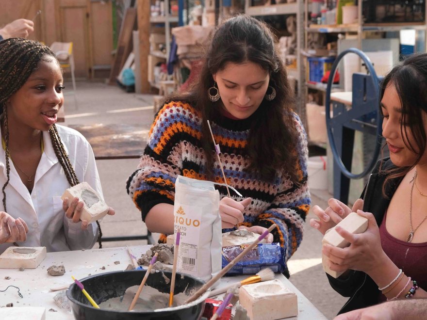 Young people sit at table and make clay objects