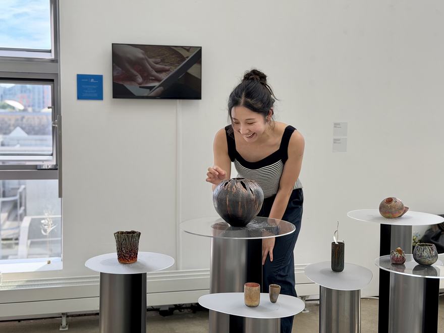 a person bends forwards to delicately examine one of several metal vessels on plinths
