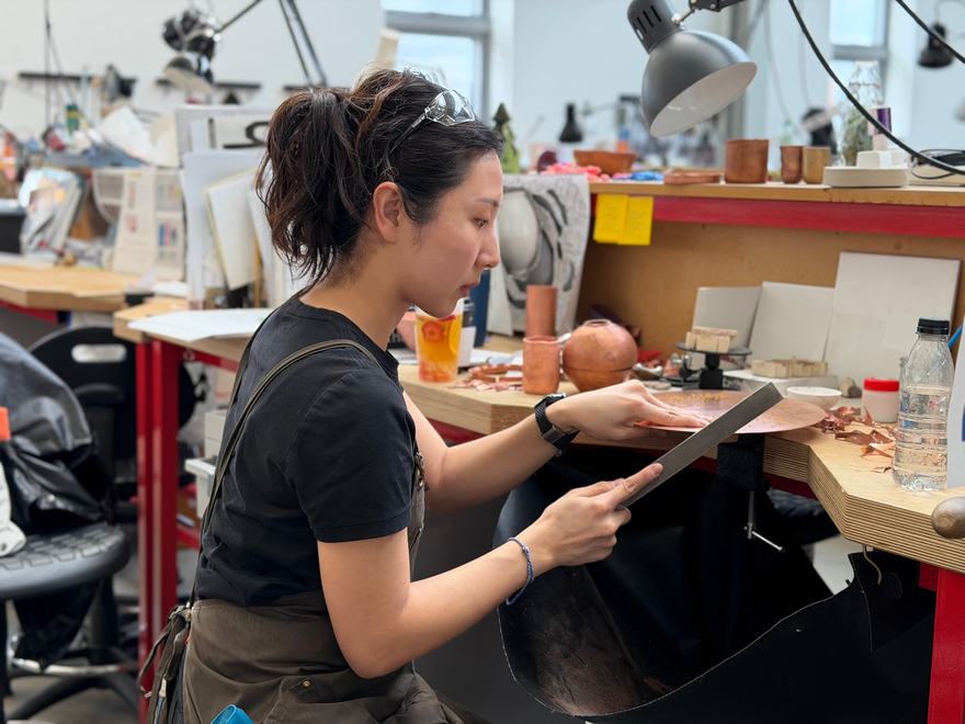 a person sits at a workbench using a file to shape edge of a copper disc