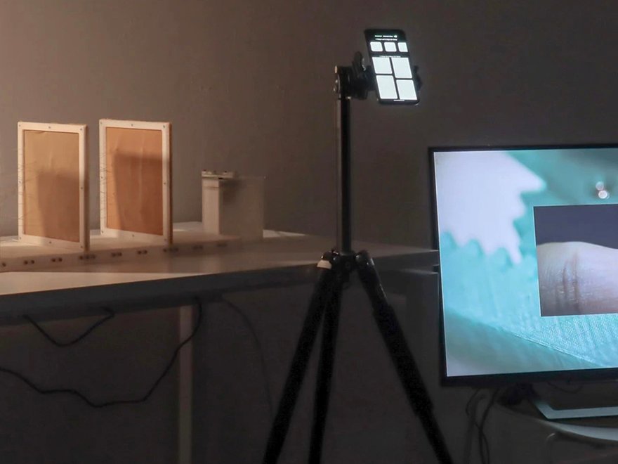 Installation shot of PickPulse, which contains textiles manipulated by metal wires connected to a smartphone, a small monitor and a large monitor (Photographer credit: Jiaqi Yang)