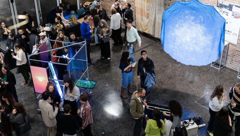 Overhead view of a crowded indoor art exhibition or event with people mingling and interacting with various installations, including a large glowing blue structure and illuminated screens.